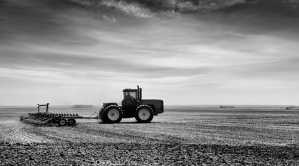 A tractor with attached cultivator working the land in a rural summer black and white countryside landscape