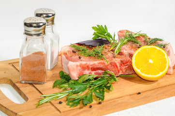 Two appetizing pieces, pork entrecote on a wooden cutting board with salt shaker and pepper and rosemary and lemon