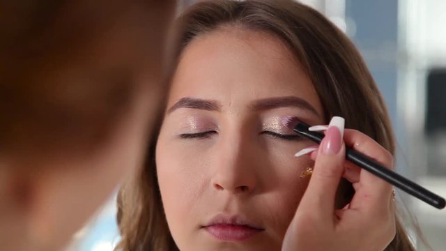 Close up of young girls's make-up process at beauty shop. Young visagiste applying eyeshadow on model's face.