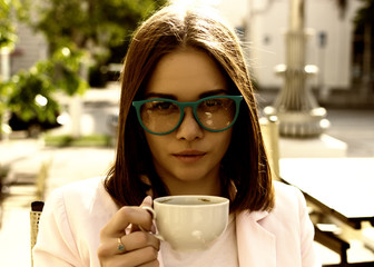 Young pretty girl drinks a cup of hot beverage, outdoor 