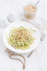 plate of vegetarian pasta with zucchini and nuts on white table, vertical, top view