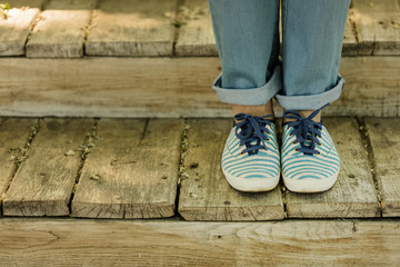 Female legs in blue jeans and striped sneakers on old wooden steps.