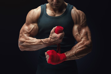 Close-up photo of strong man wrap hands on black background Man is wrapping hands with red boxing...