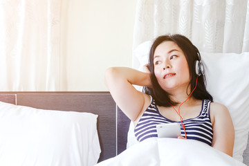 Woman listening music with headphones on bed
