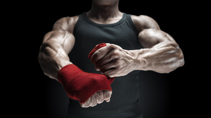 Obraz na płótnie Canvas Close-up photo of strong man wrap hands on black background Man is wrapping hands with red boxing wraps isolated on black background Strong hands and fist, ready for training and active exercise
