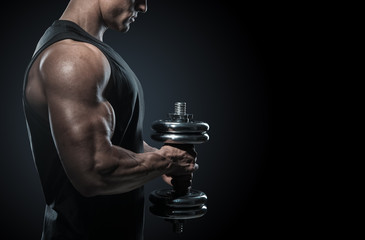 Handsome power athletic man in training pumping up muscles with dumbbell