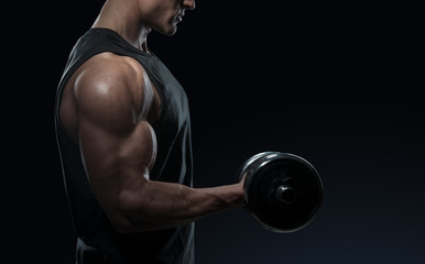 Handsome power athletic man in training pumping up muscles with dumbbell. Strong bodybuilder with perfect deltoid muscles, shoulders, biceps, triceps and chest. Close-up of a power fitness man. - obrazy, fototapety, plakaty