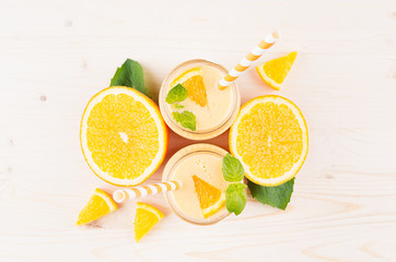 Decorative border of orange citrus smoothie in glass jars with straw, mint leaf,  cut orange, top view. White wooden board background, copy space.