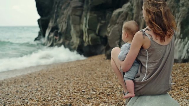 Mother and baby on the beach looking at the waves