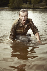 Wet and dirty soldier in uniform overcomes hardly river