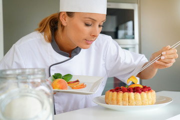 Pastry chef in professional kitchen decorating raspberry cake with fruits