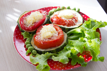 Appetizer of zucchini and tomatoes, baked with cheese on lettuce leaves with green peas.  Selective focus. Top view.