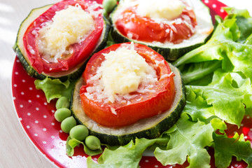 Appetizer of zucchini and tomatoes, baked with cheese on lettuce leaves with green peas. Close-up. Selective focus.