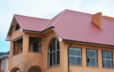 New metal roofing construction with rain gutter system guttering, brick chimney and Attic, mansard roof repair.