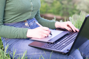 Naklejka premium Young girl using her graphic tablet sitting in the grass