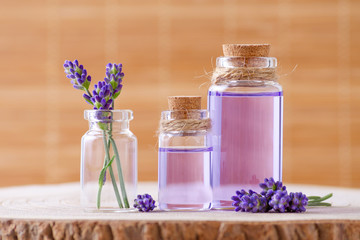 Fototapeta na wymiar essential oil in glass bottles and fresh lavender flowers on stump and brown background