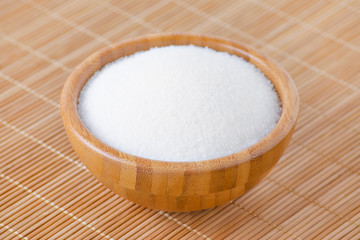 a wooden bowl with white sugar on bamboo texture