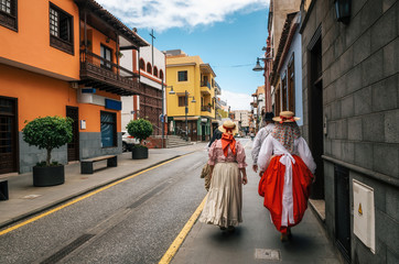 A group of locals in Canarian traditional clothes walk along the street of Puerto de la Cruz with colorful houses. Celebration of the Day of Canary Islands. View from the back. Tenerife, 30 may, Spain