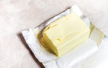 Creamy butter in its unwrapped foil paper. Isolated on light table
