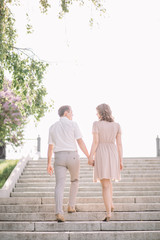 beautiful couple on a walk, the girl in the beige dress and the guy wearing light clothing go up the stairs back, holding hands, Park, summer, nature