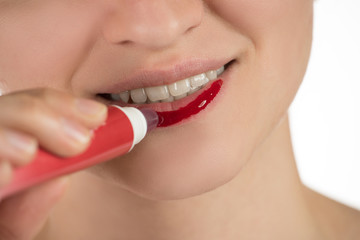 A beautiful young girl applies a persistent liquid red lipstick from a tube to her lips, and then takes it off as a film