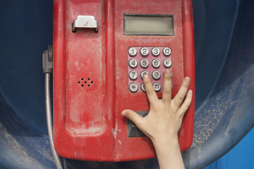 A small child's hand dials a phone number on a street phone. Protection of the rights of the child. Child abuse