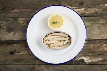 Can of preserved with clams on a plate on a rustic wooden table.