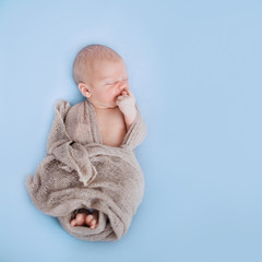 Studio shoot of cute 10 days old newborn baby sleeping on a soft blue blanket in a wrap