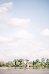 love story, beautiful couple a man and a woman in bright clothes, dress walking along the river Bank,are holding hands, vertical, blue sky with white clouds, summer, nature