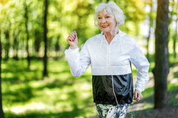 Jolly senior woman enjoying running in forest