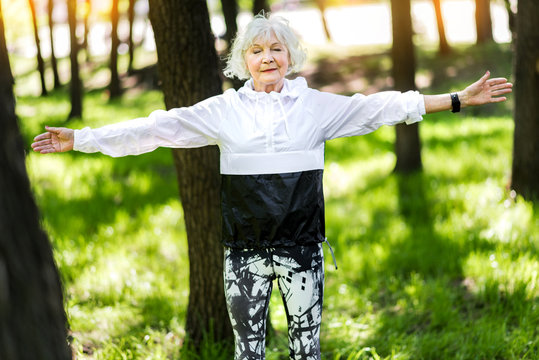 Happy old woman doing relaxation exercises in summer park