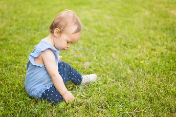 Fourteen months old baby girl sitting in the shadow on the grass on the sunny summer day