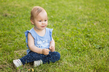 Fourteen months old baby girl sitting in the shadow on the grass on the sunny summer day