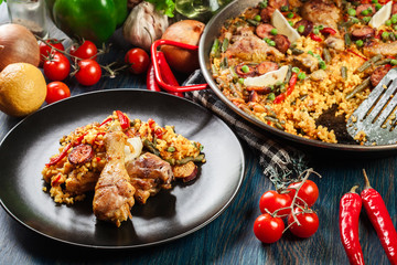 Traditional paella with chicken legs, sausage chorizo and vegetables served on black plate
