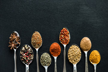 top view of various spices and herbs in metal spoons isolated on black
