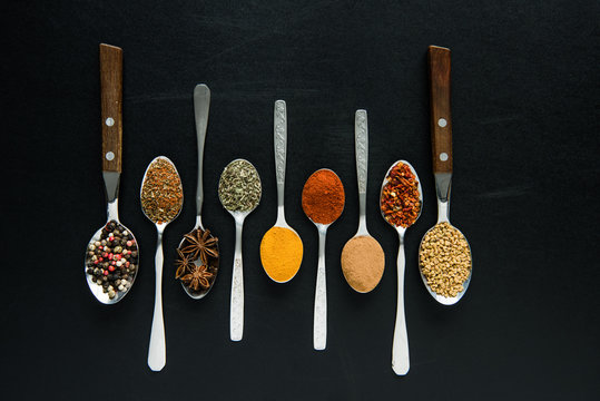 top view of various spices and herbs in metal spoons isolated on black