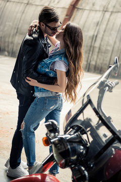 Stylish young couple hugging and kissing while standing near motorbike
