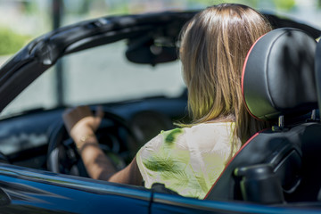 Young blond woman driving a convertible car stopped at a light.