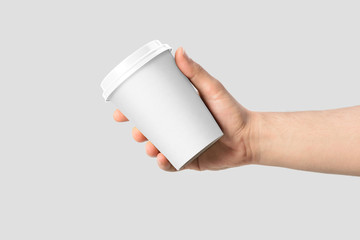 Mockup of male hand holding a Coffee paper cup isolated on light grey background. 