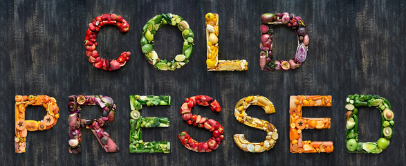 Cold pressed juice vegetables words spelled out with healthy organic fruit on rustic background