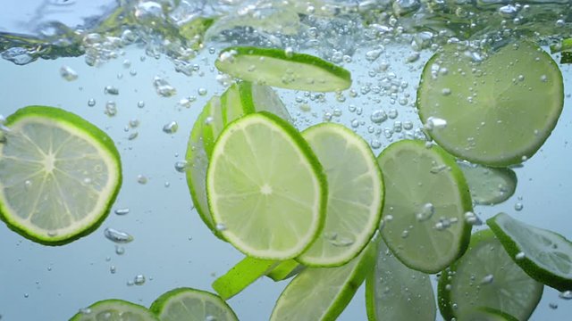 Fresh lime slices fall Into water and float with bubbles slow motion.