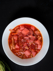 Traditional red soup - borscht in a white plate on a black background.Top view