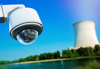 closeup image of CCTV security camera and blurred atomic power plant on background