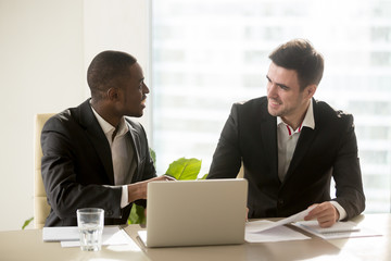 Two accomplished multiracial businessmen discussing idea new business projects at office desk, multi ethnic business group having pleasant funny conversation indoors, running company together