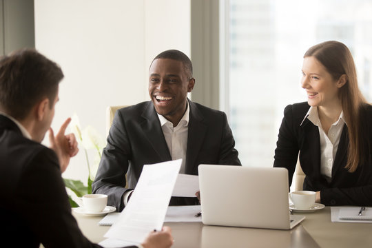Handsome afro american businessman with beaming smile laughing on multi-ethnic international team meeting when partner telling joke, cheerful diverse business people having fun friendly atmosphere