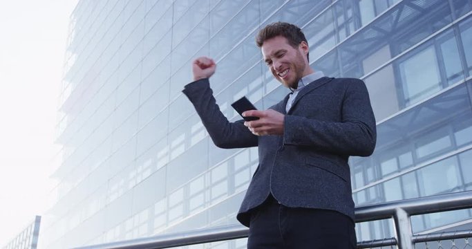 Business success and achievement - happy businessman cheering celebrating on cell phone. Young urban professional successful business man reaching personal goals. Smartphone app or video game concept.