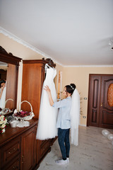 Beautiful bride looking at her white gorgeous wedding dress in her room.