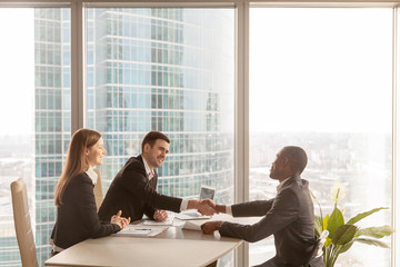 Friendly caucasian employers and confident african-american applicant handshaking during job...