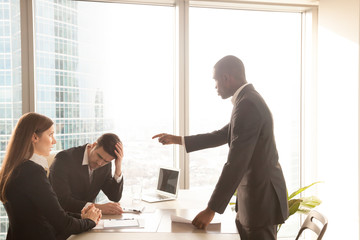 Angry bad african american boss yelling at caucasian employees, receiving reprimand with guilty and...