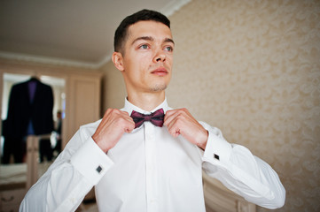 Groom tie his bow tie at room.